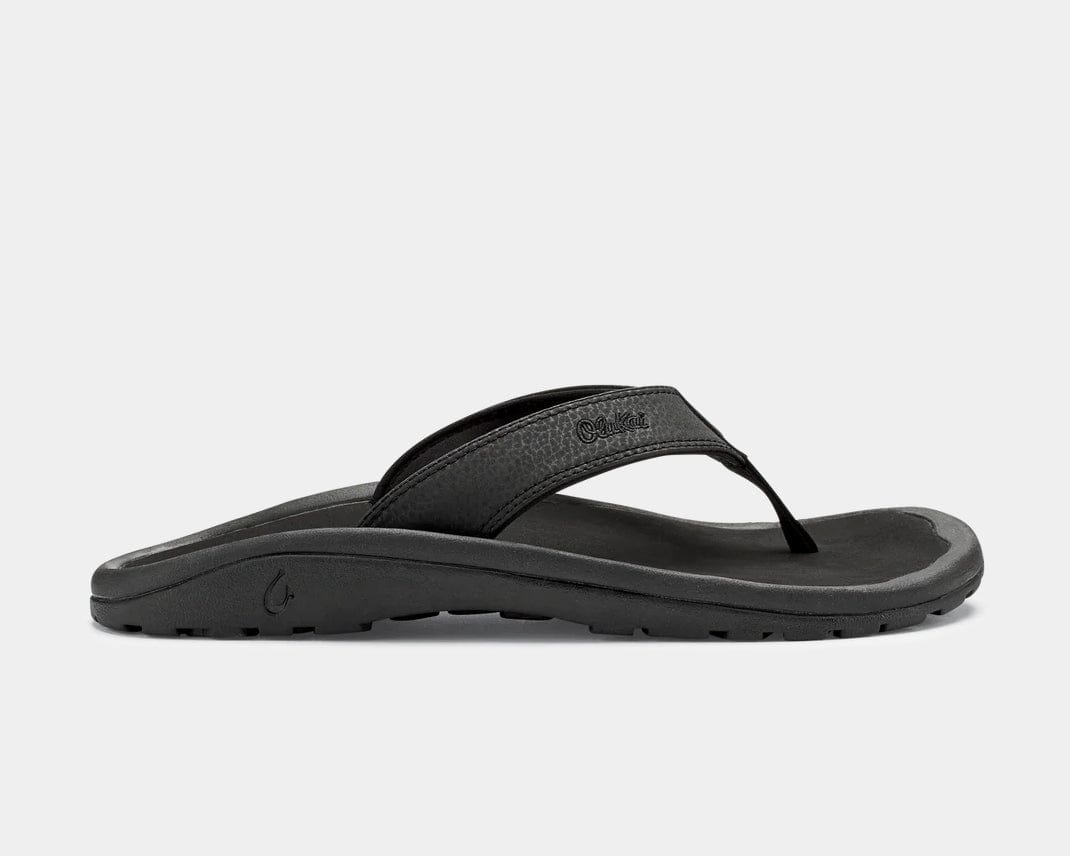 A pair of black Ohana sandals by Olukai, featuring a water-resistant synthetic strap and a non-marking rubber outsole with a coral reef lug design.
