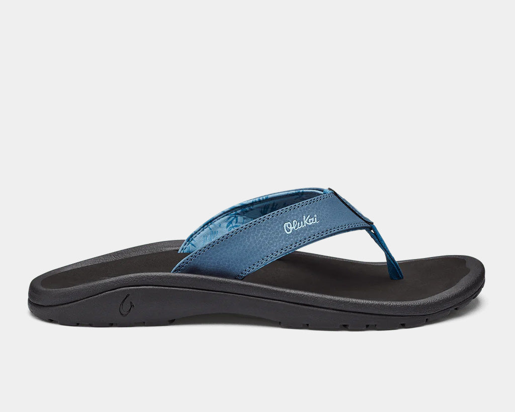 A pair of blue Ohana sandals by Olukai, featuring a water-resistant synthetic strap and a non-marking rubber outsole with a coral reef lug design.