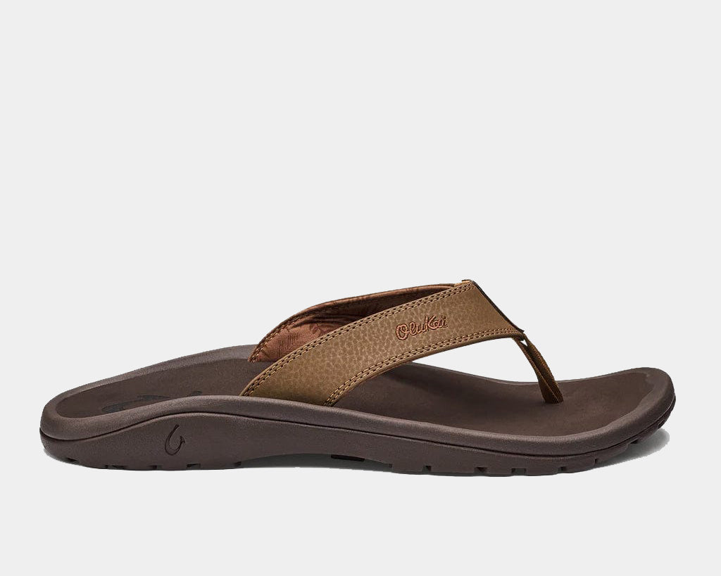 A pair of brown Ohana sandals by Olukai, featuring a water-resistant synthetic strap and a non-marking rubber outsole with a coral reef lug design.