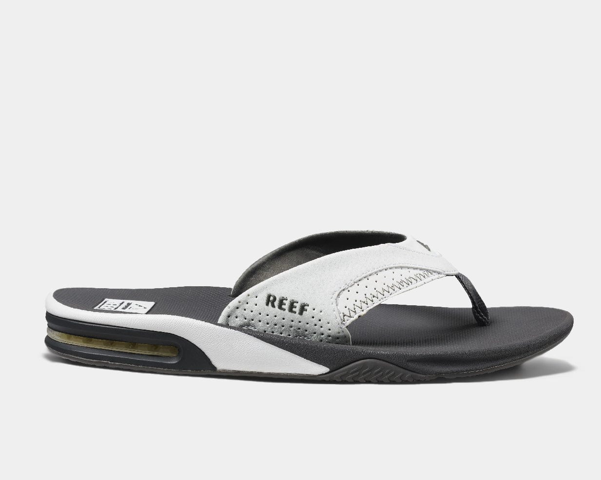 A pair of Reef leather flip flops with a contoured black and white footbed, featuring a bottle opener built into the heel, and branded with the Reef logo.