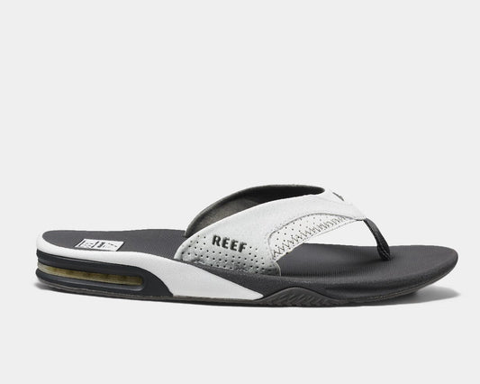 A pair of Reef leather flip flops with a contoured black and white footbed, featuring a bottle opener built into the heel, and branded with the Reef logo.